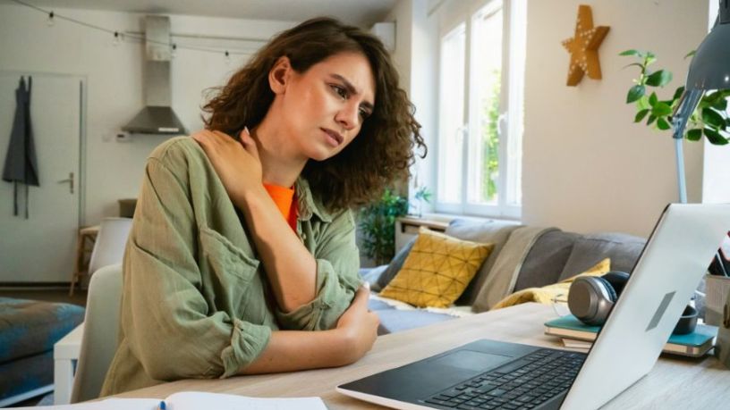 A woman sits at her desk, holding her sore shoulder.
