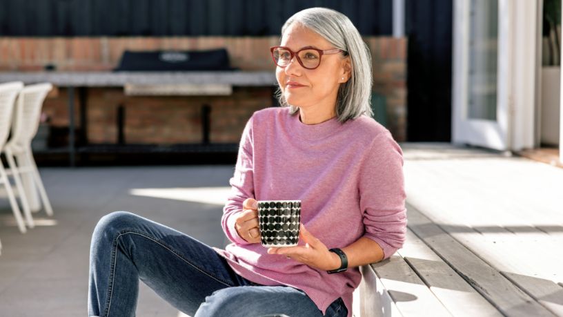 A woman holding a coffee mug sits in a backyard.