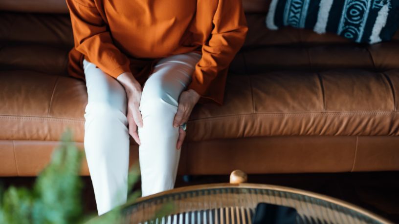 A woman on a couch holds her sore knee.