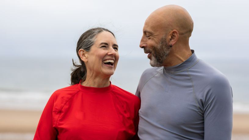 A man and woman laugh at the beach.