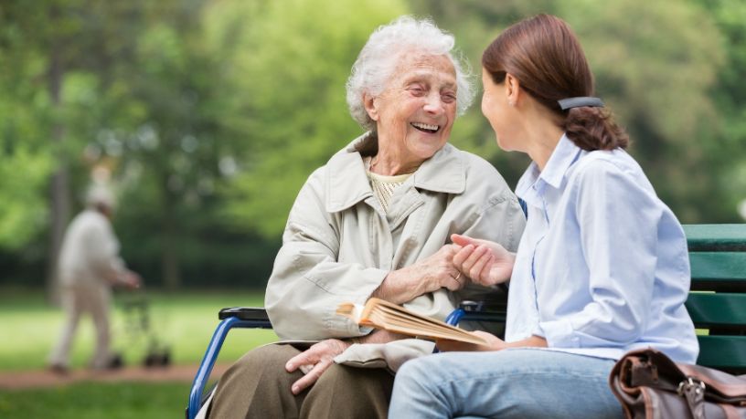 A health professional talks with a woman in a walker as the pair sit in a park.