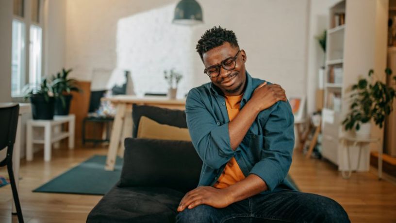 A man sits on a lounge chair, grimacing and holding his shoulder.