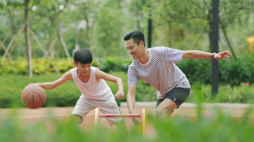 A father and son play basketball in the park.