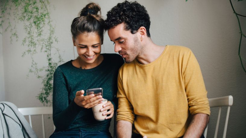 Two younger people looking at a phone and smiling.
