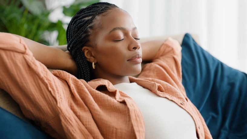 A woman relaxes on a couch with her hands behind her head.