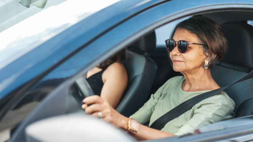 A woman wearing sunglasses drives her car.