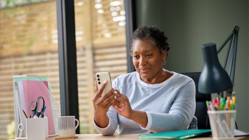 A woman sitting at her desk looking at her phone.