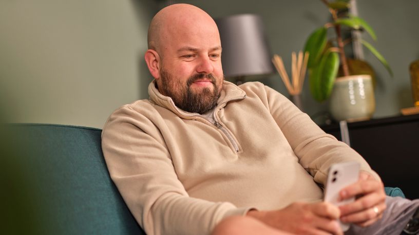 A man relaxes on a couch and reads from his phone.