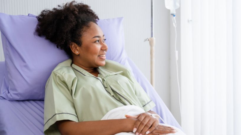 A woman lies in a hospital bed, looking out of a window.