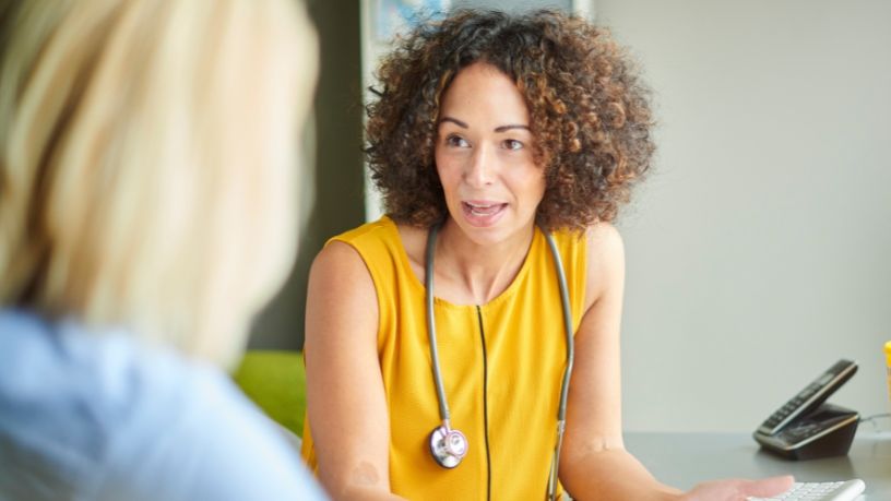 A doctor sits at her desk speaking to her patient