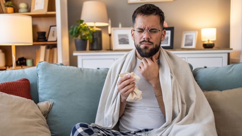 A man winces while holding one hand to his throat and tissues in the other.