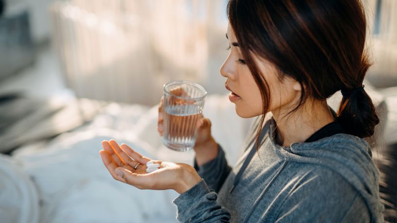 Lady with a glass of water about to swallow 2 tablets.
