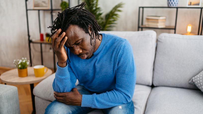A man sits on his couch lightly touching his hand to his sore face.