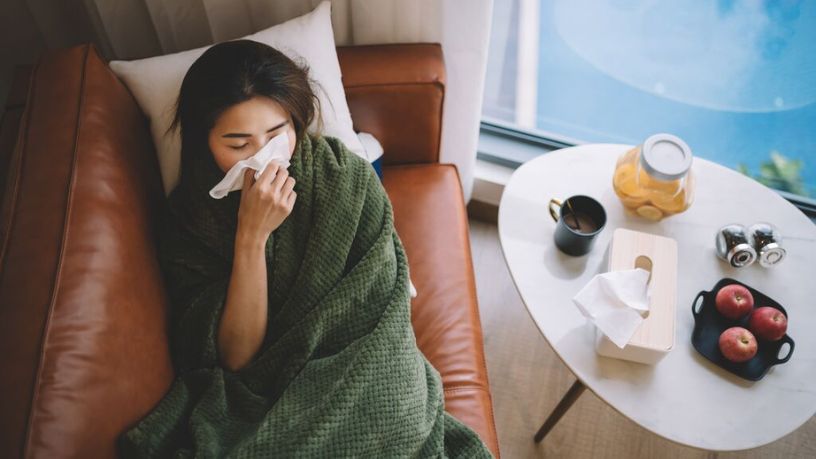 A woman laying on the couch recovering from a cold or flu.
