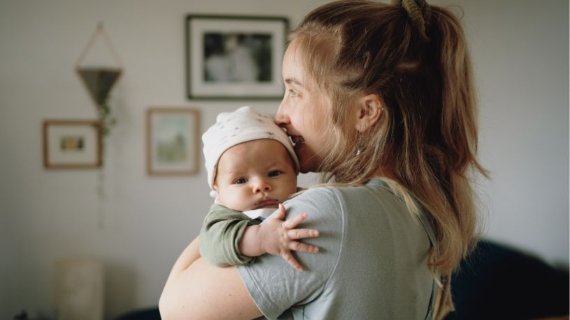 A woman cuddles her baby in her living room.