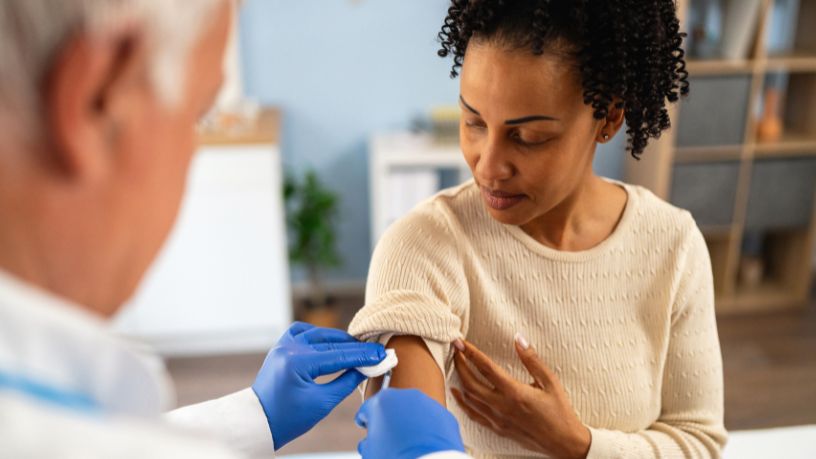 A doctor applies a cotton bud while removing a needle from a woman's arm.