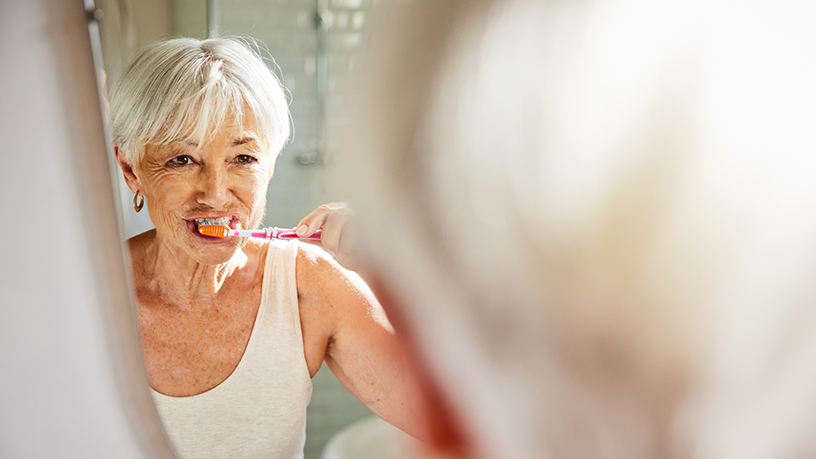 A woman looking directly into the mirror while brushing her teeth.