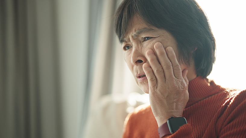 A woman holding her cheek with a sore jaw.