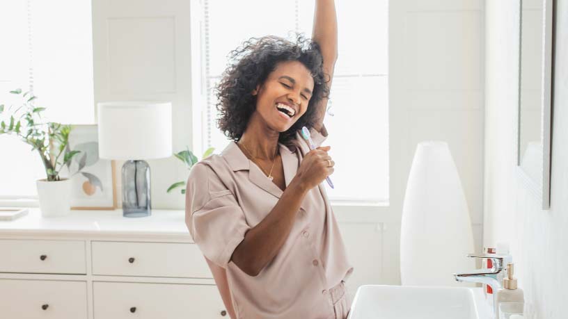 A woman uses her toothbrush to sing in front of her bathroom mirror.