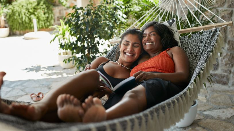 Two women laugh on a hammock.