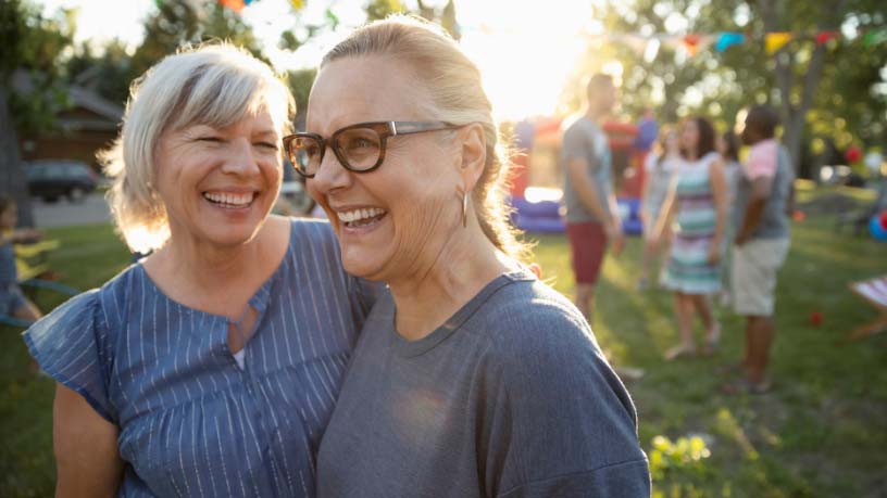 Two women laugh together at a party in a park.