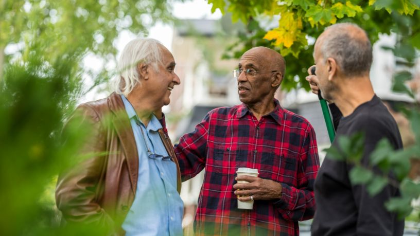 A group of older men smile and chat in a park.