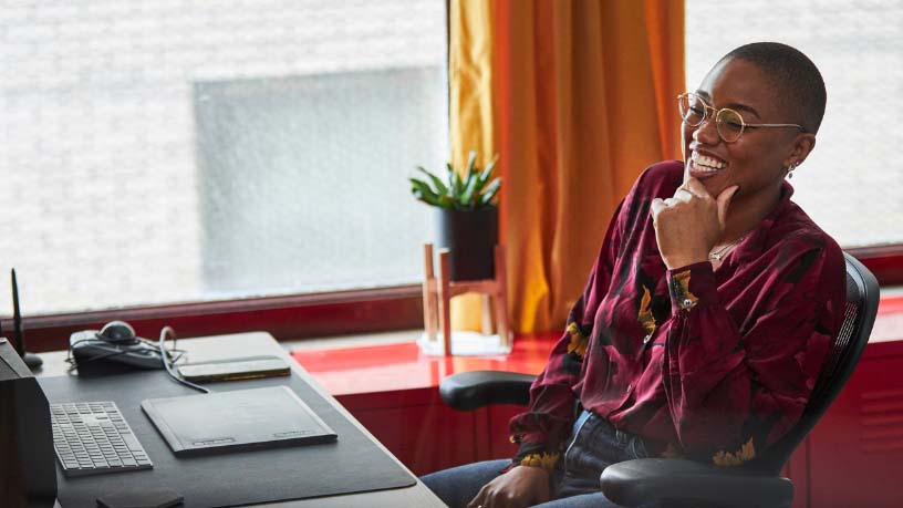 A woman wearing glasses grins while in a meeting on her computer.