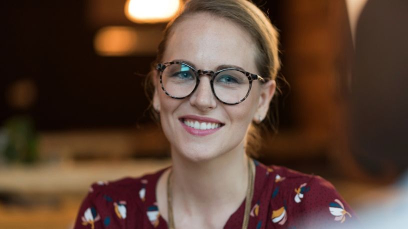 A woman wearing glasses looks towards something off-camera.