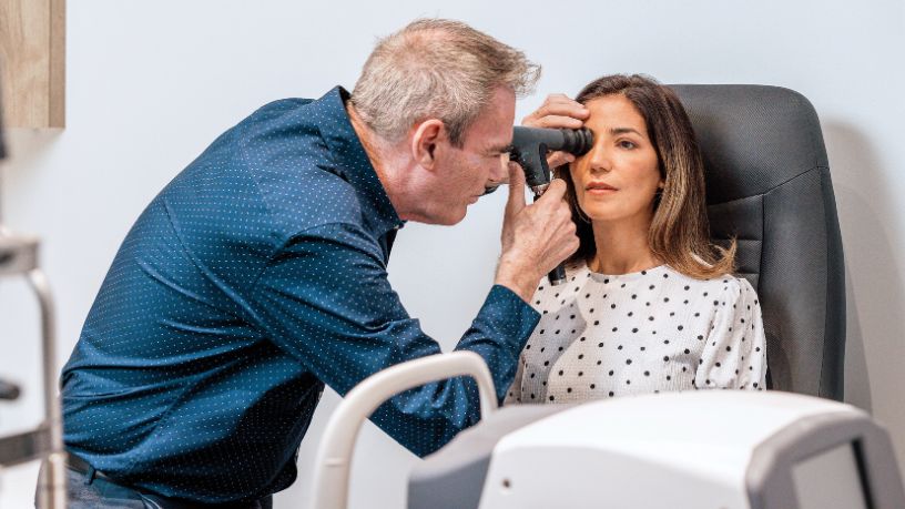 An optician uses a scope to check a woman's eye.