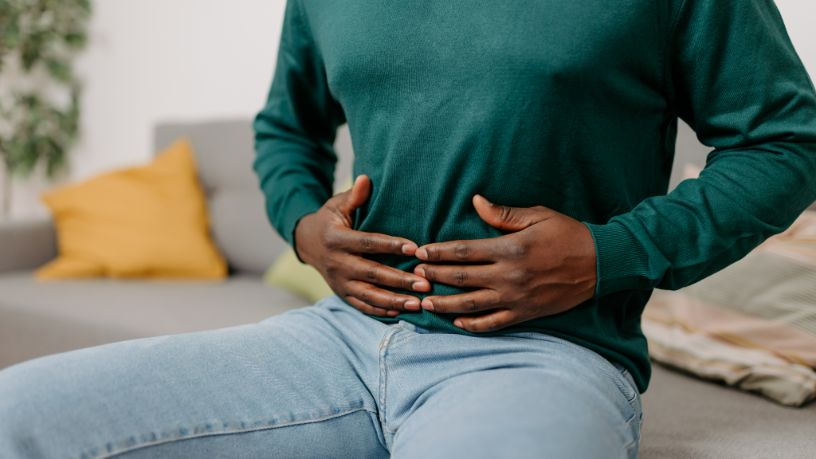 A man sitting on his couch holds his stomach gently.