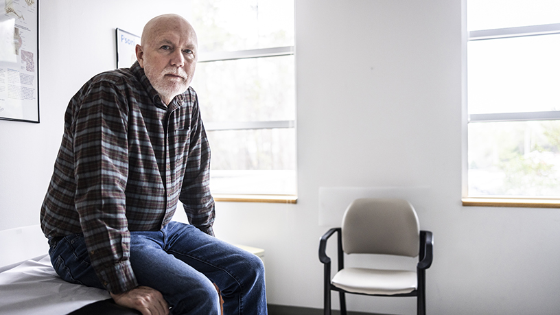 A man sitting on the edge of a hospital bed with a faraway stare.