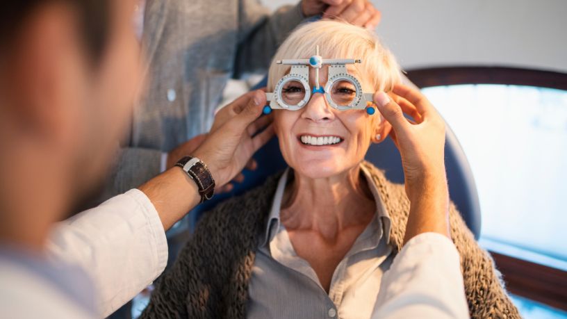 An optometrist holds a pair of trial frame lenses to his patient's eyes.
