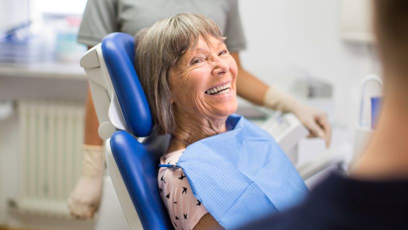 An older woman on a dentist's chair grins, showing off her teeth.