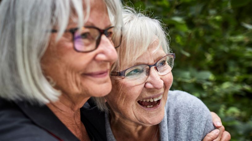 Two older women hug and laugh together.