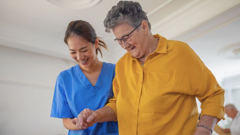 A medical professional helps a woman to walk, holding her hand.