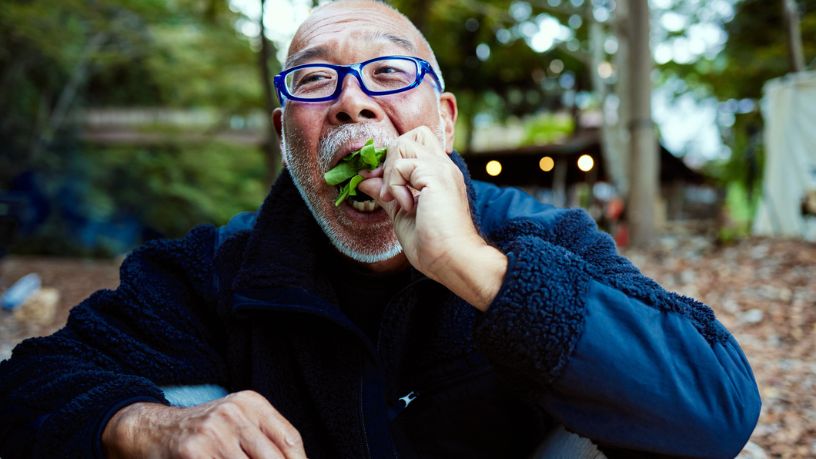 An older man smiling and eating salad.