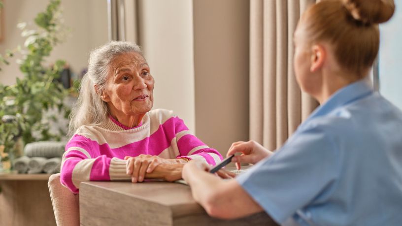 An older woman sits at a table speaking with a medical professional.