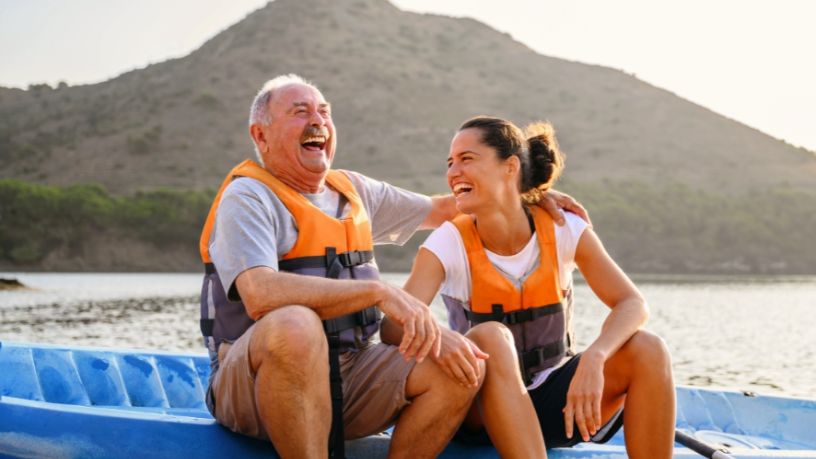 A laughing man and woman sit side by side on a lakeside kayak.