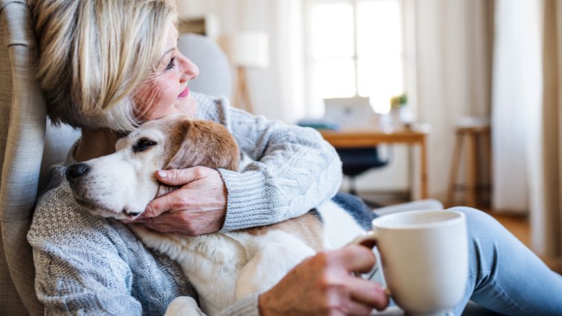 Woman on the couch with a cup of tea and her dog on her lap.