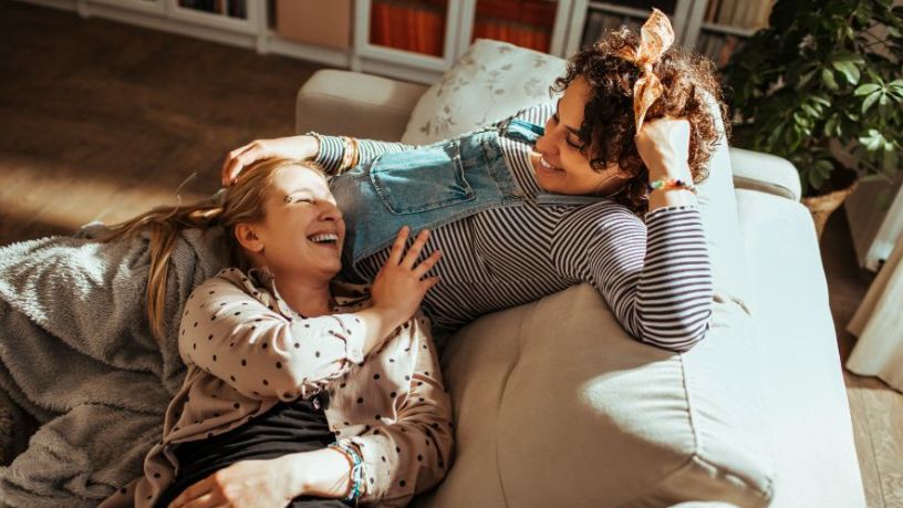 Pregnant couple lay on the couch laughing.