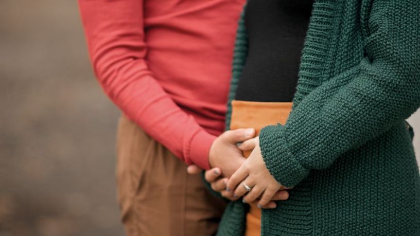 Two people hold their hands against a pregnant belly.