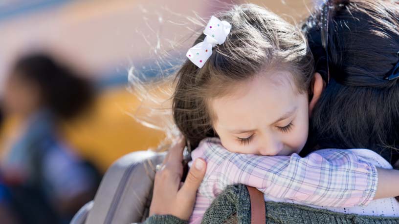 A little girl hugs her mum at school.