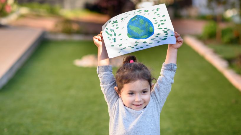 A little girl holds a drawing of Earth above her head