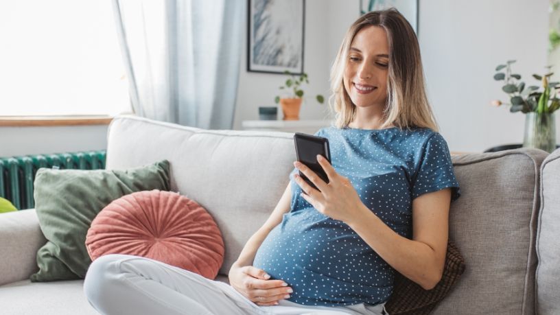Pregnant woman sitting on the couch looking at her phone.