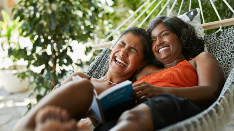 Two women sitting in a hammock laughing.