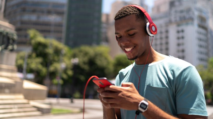 A man wearing headphones smiles as he texts on his phone.