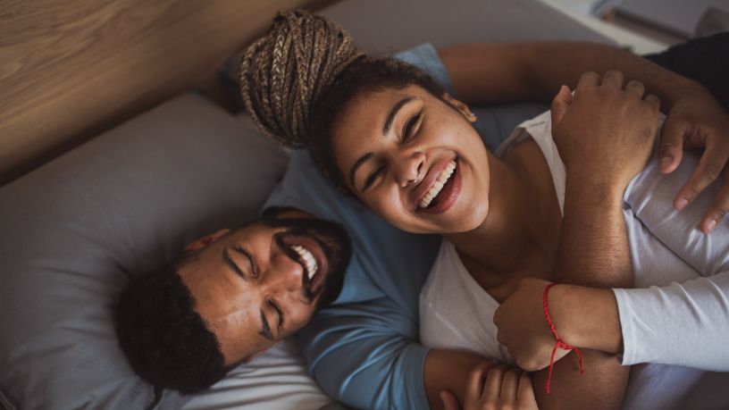 A man and woman embrace on their bed and laugh