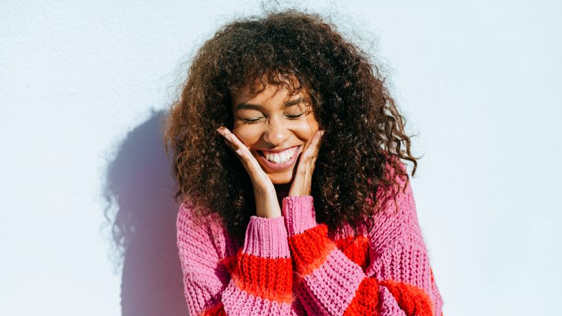 An overjoyed woman presses her face between her hands.