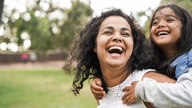 A woman with her daughter on her back smiling.