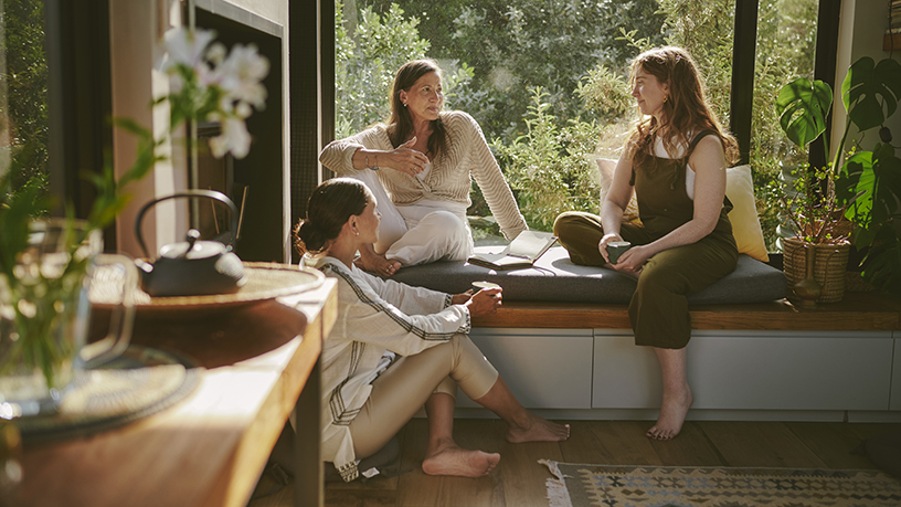 Three women talking together at a window seat.